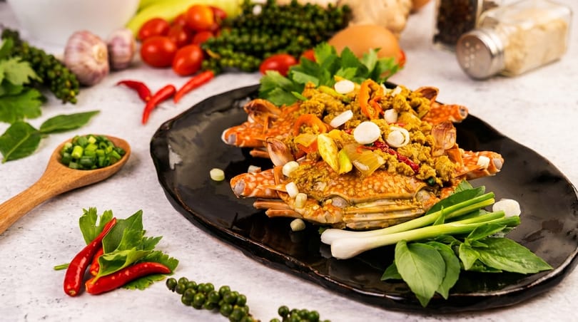 Spicy Thai stir-fried crab with curry powder, spring onions, and basil on a black plate.