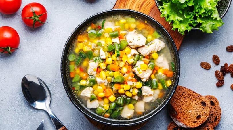 Hearty chicken and vegetable soup with corn, green beans, carrots, and celery, garnished with fresh tomatoes and lettuce.