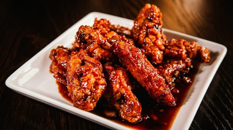 A white rectangular plate filled with glistening, saucy chicken wings on a dark wooden table.