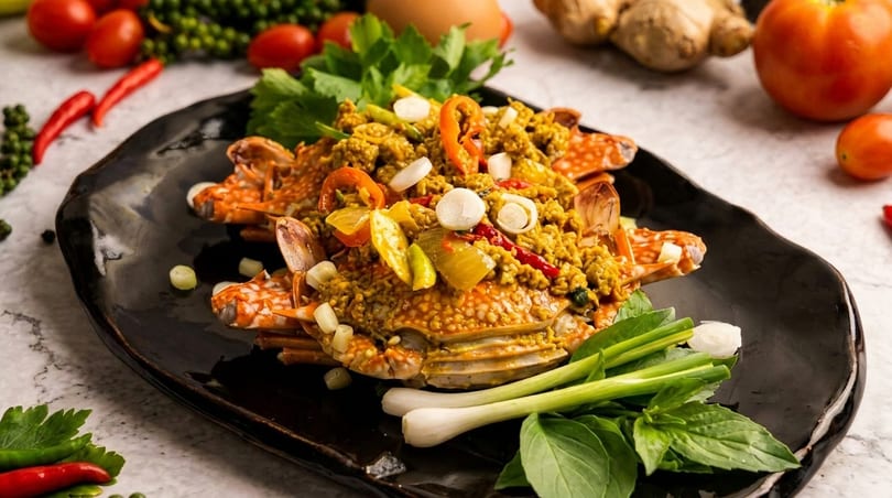 Spicy stir-fried crab with yellow curry paste, chili, and herbs on a black plate.