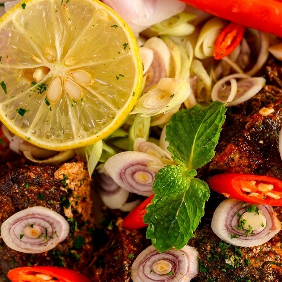 Close-up of spicy fish with lemon, red chilies, sliced onions, and fresh herbs.
